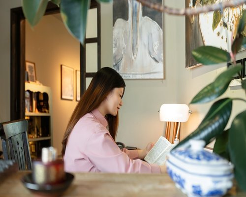 Person reading a physical book with a warm desk lamp